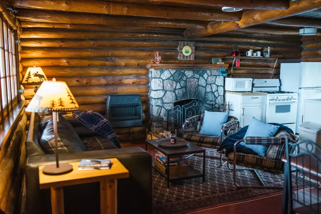 living room and kitchen in log cabin with couch, chairs and fireplace